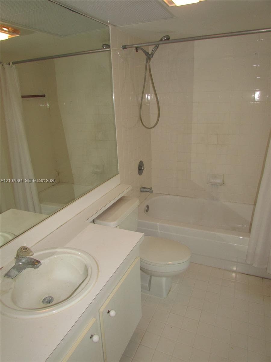 Full-width vanity with integrated sink, expansive wall-mounted mirror, white ceramic tile flooring, and a combined tub and shower enclosure with a handheld fixture