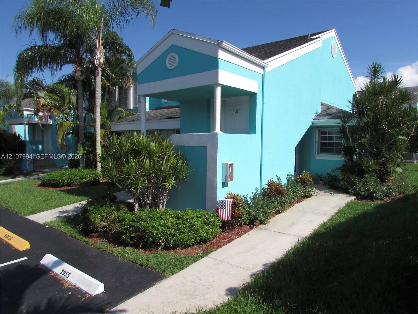 Stucco exterior featuring a covered entryway with column support, gable roofline, concrete walkway, and landscaped garden beds