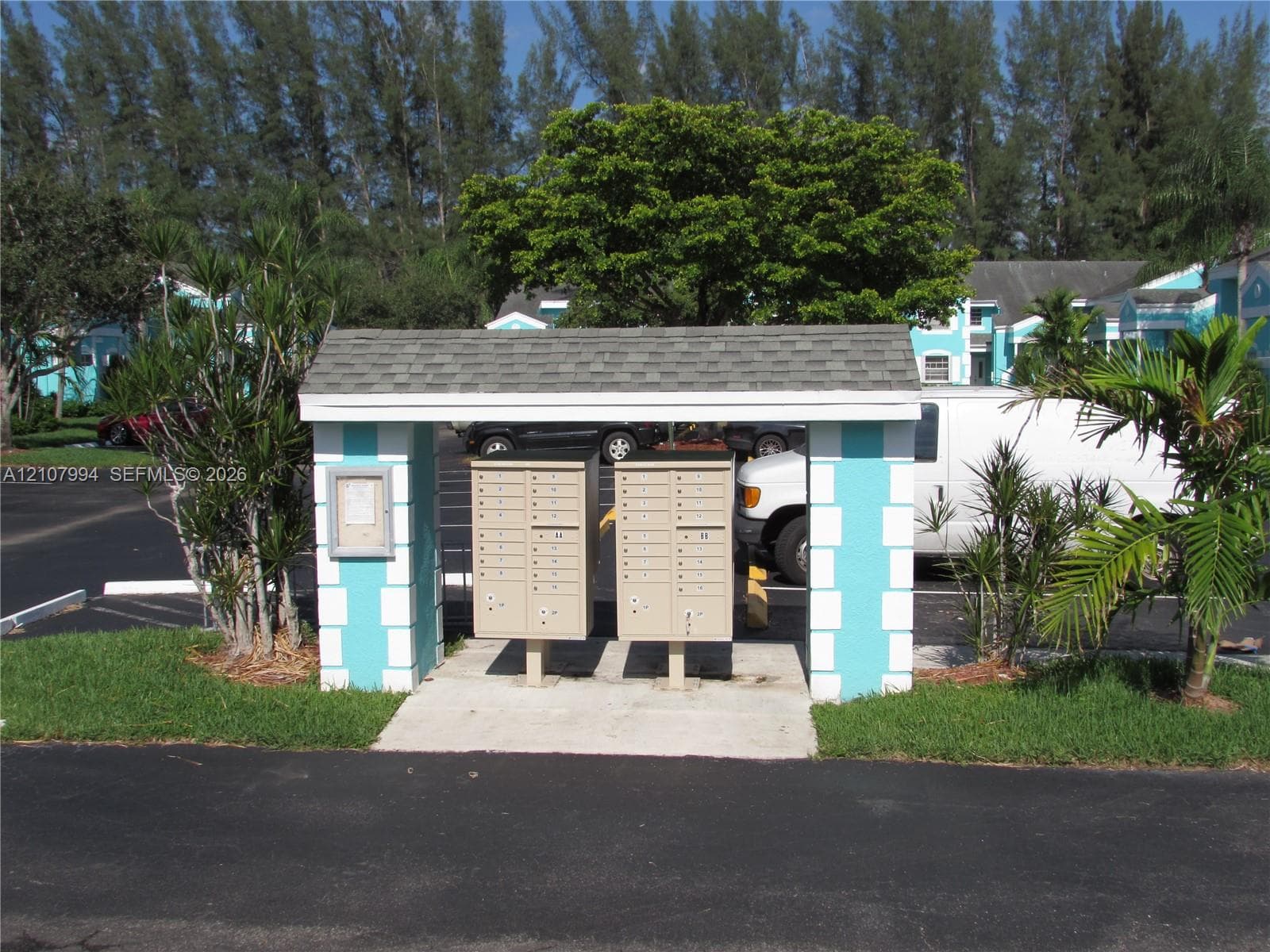 Covered mail station featuring twin metallic parcel units, concrete foundation, and decorative block pillars with shingled roofing