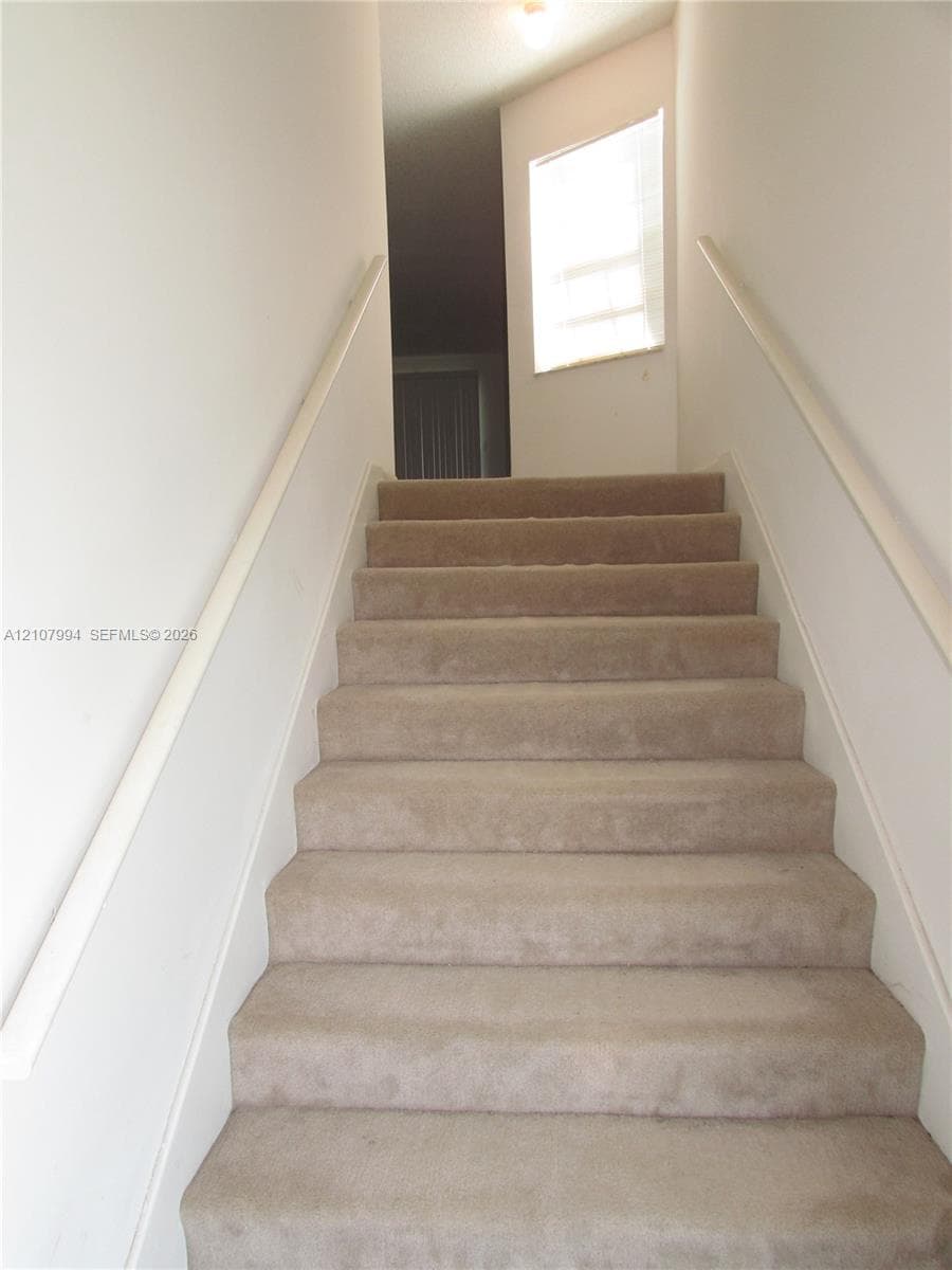 Carpeted staircase featuring dual white handrails and a window at the landing