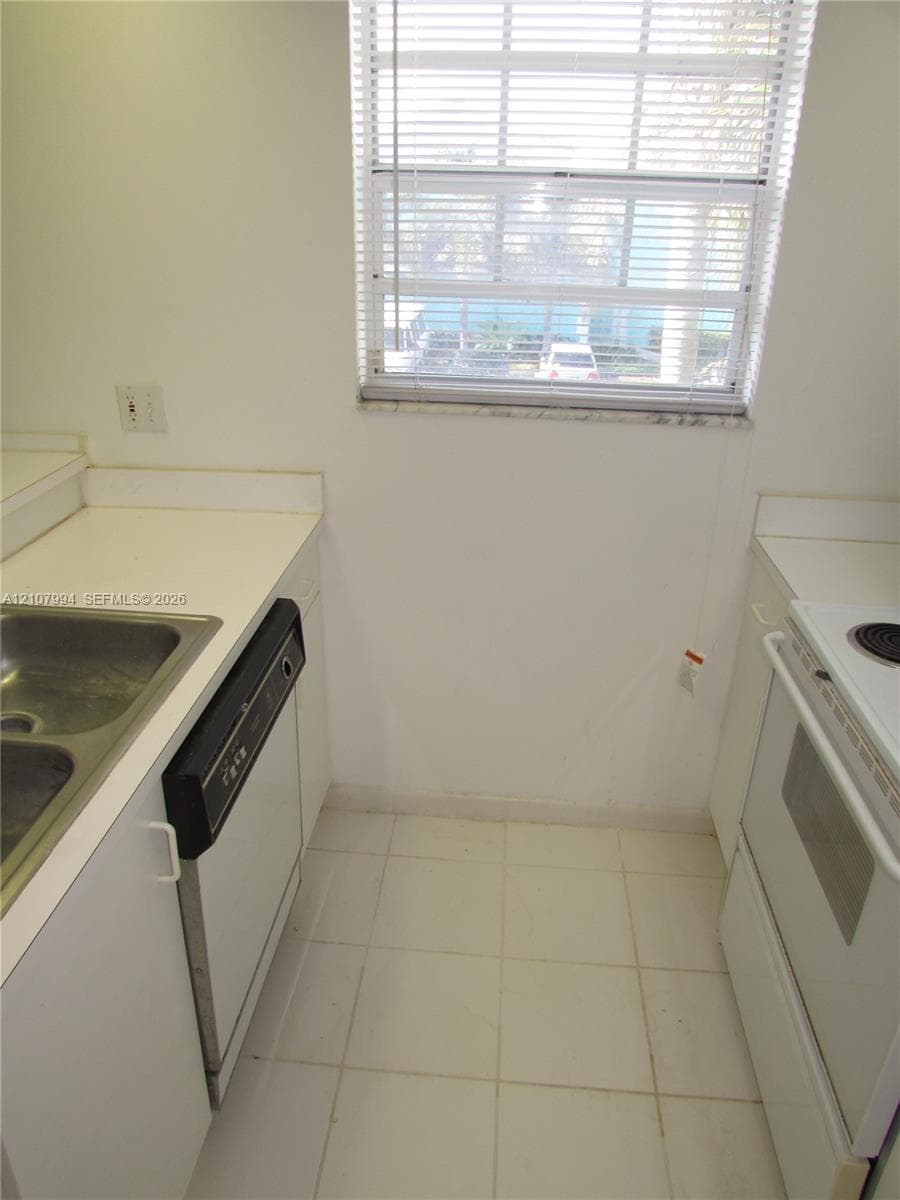 Kitchen featuring white cabinetry, solid-surface countertops, dual-basin stainless steel sink, integrated dishwasher, and tile flooring