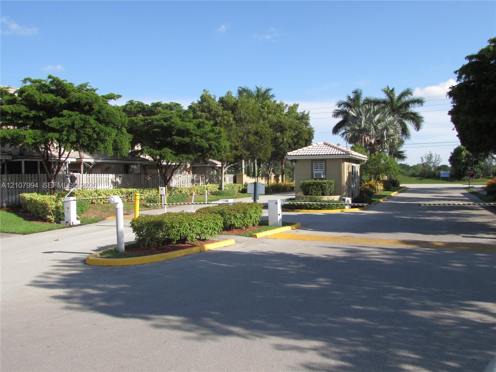 Gated entry featuring a controlled-access security station, paved driveway, and mature landscaping