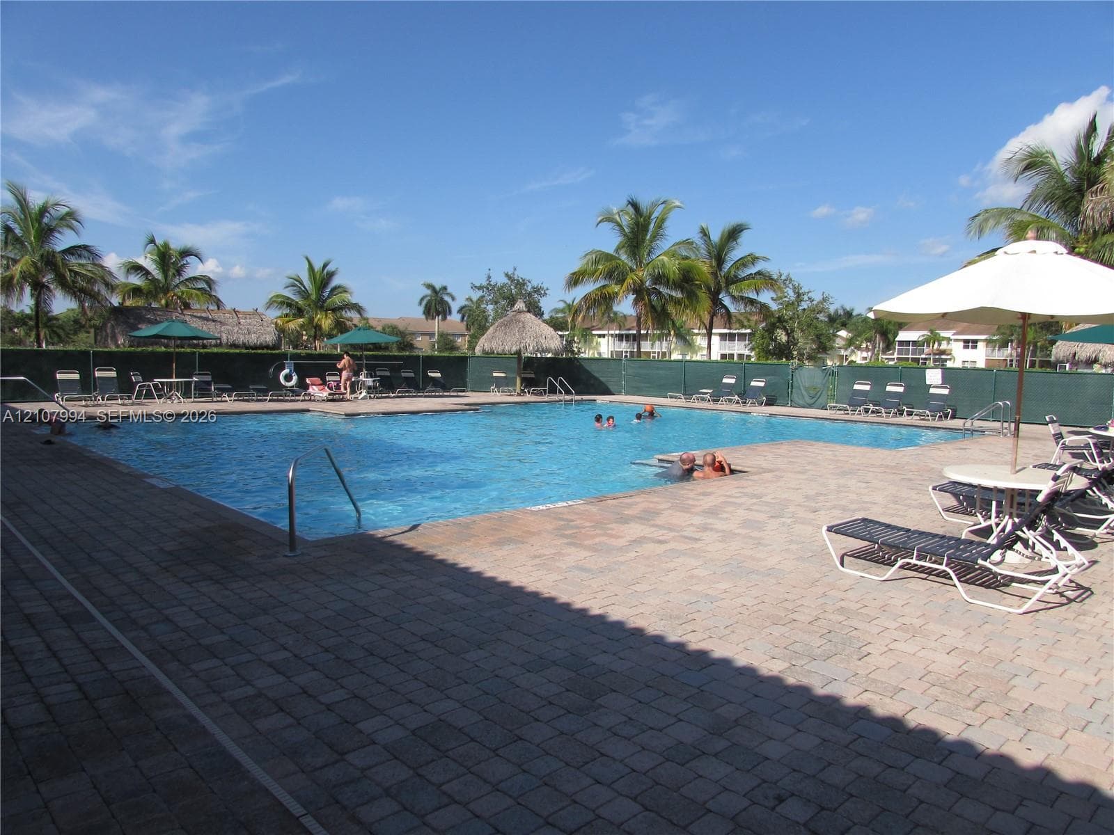 Swimming pool featuring a paver deck, metal handrails, and tropical landscaping