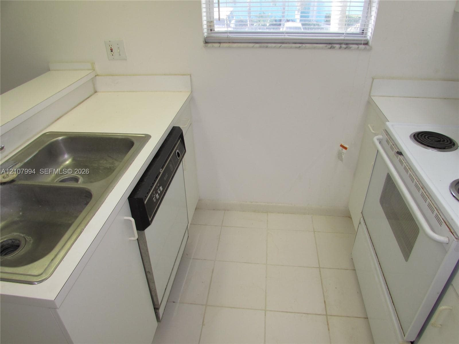 Kitchen featuring solid-surface countertops, dual-basin stainless steel sink, white cabinetry, built-in dishwasher, and ceramic tile flooring