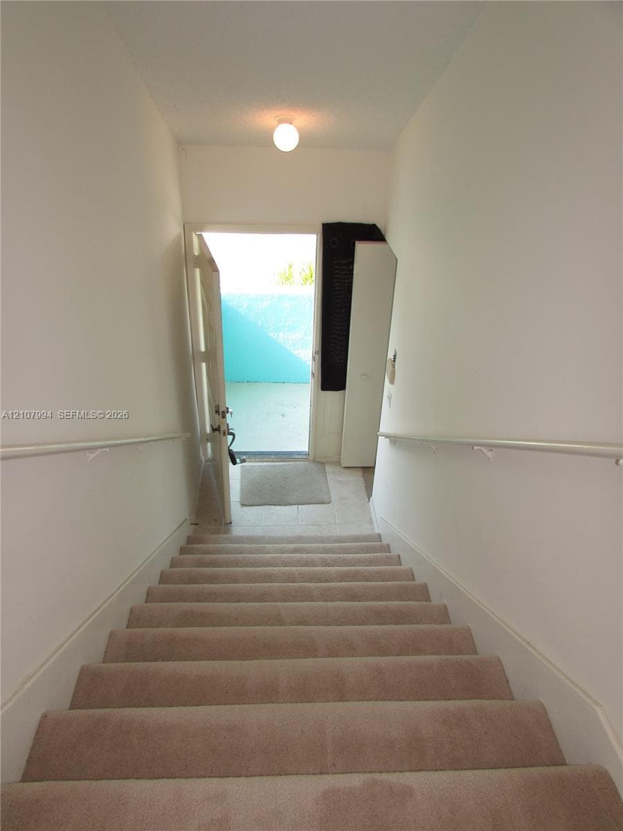 Carpeted staircase featuring white handrails and a flush-mount ceiling light fixture