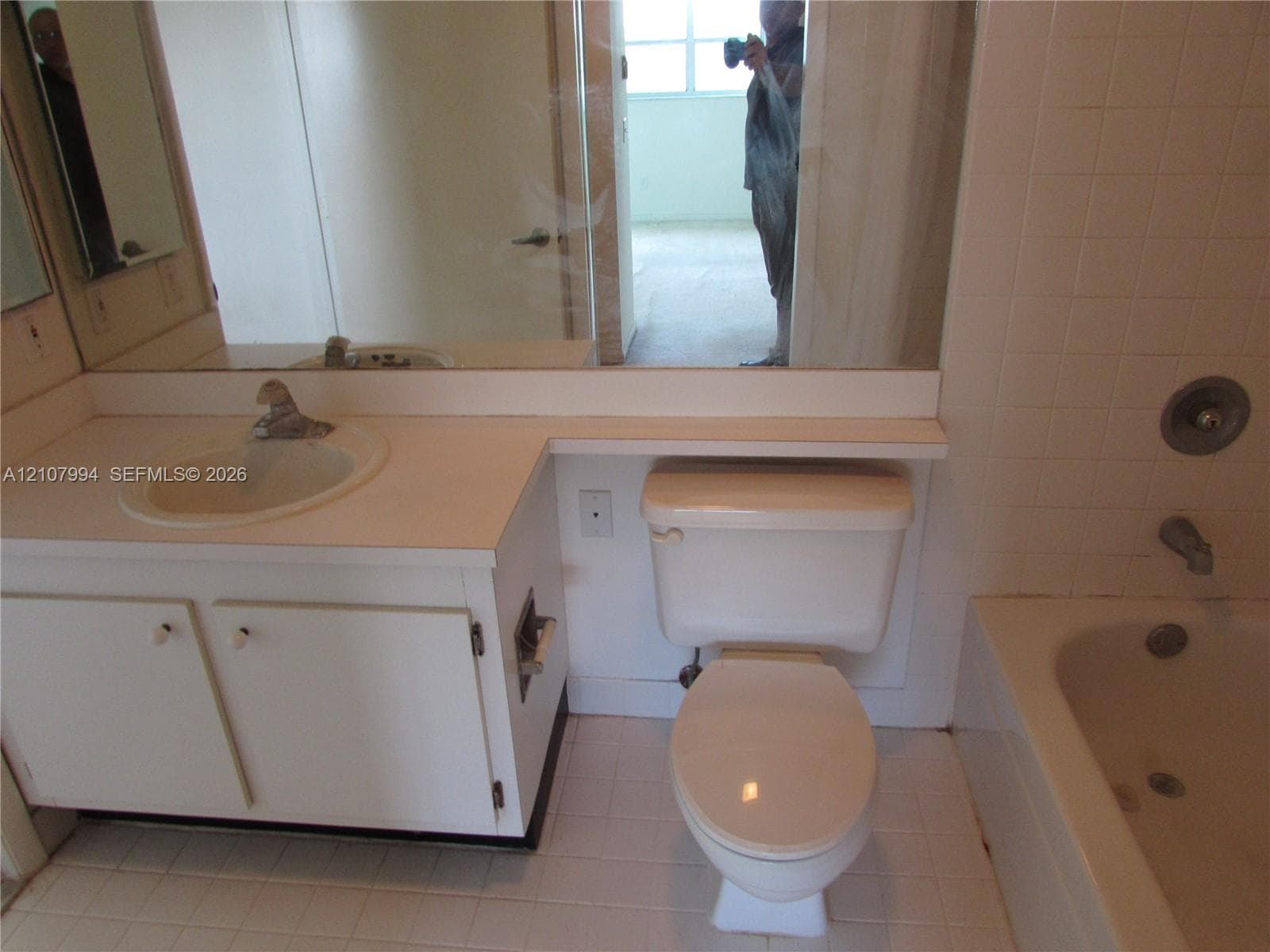Bathroom featuring a white vanity cabinet with an integrated sink, large wall-mounted mirror, white ceramic tile tub surround, and tile flooring