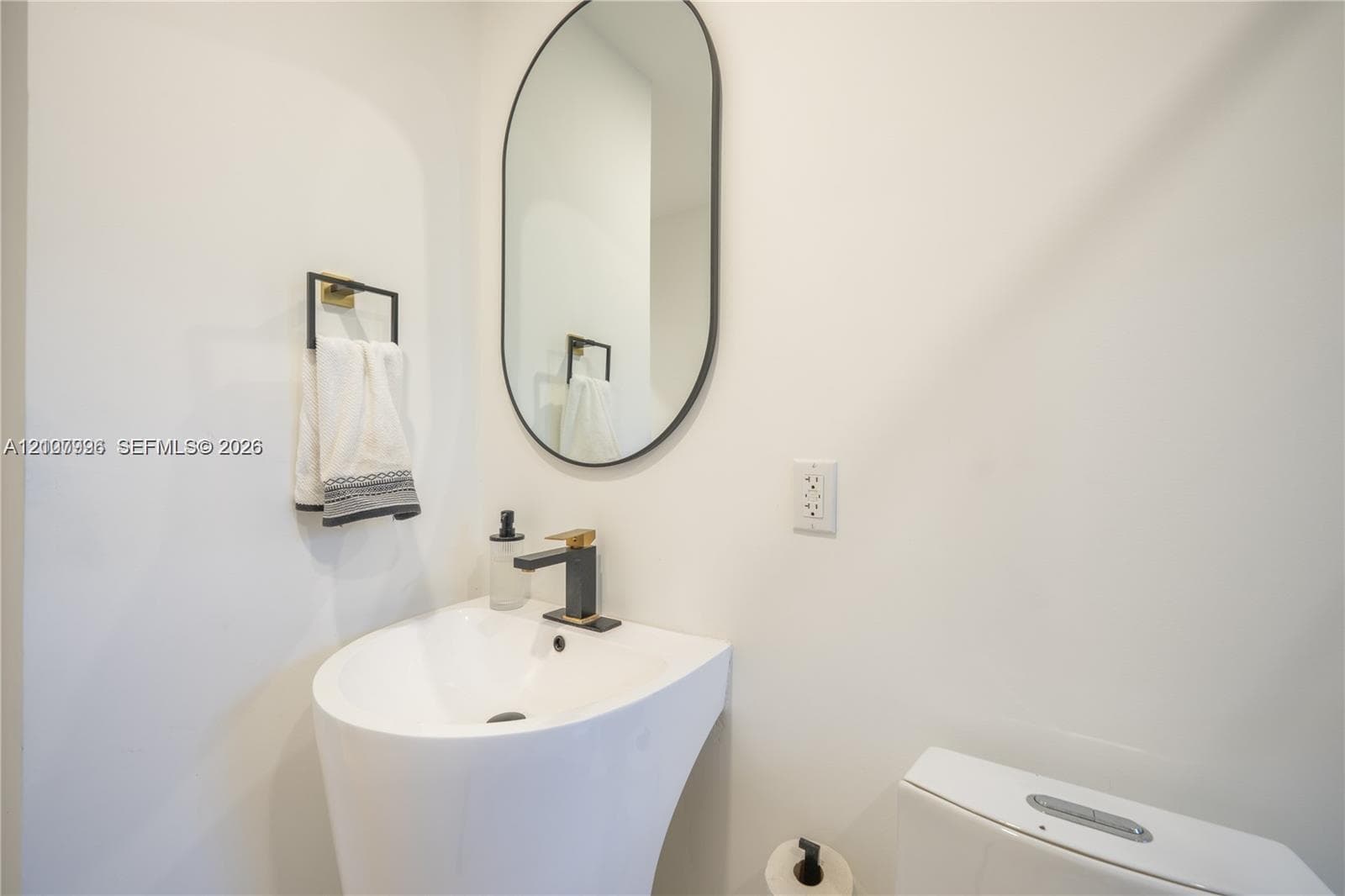 Pedestal sink featuring a matte black faucet, oval wall-mounted mirror, and wall-mounted towel ring