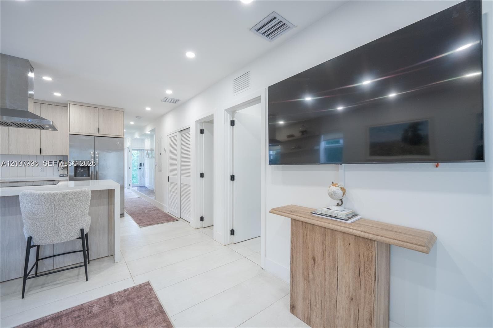 Kitchen featuring light-tone cabinetry, stainless steel appliances, a range hood, and a quartz-topped peninsula with bar seating, complemented by large-format tile flooring and recessed lighting