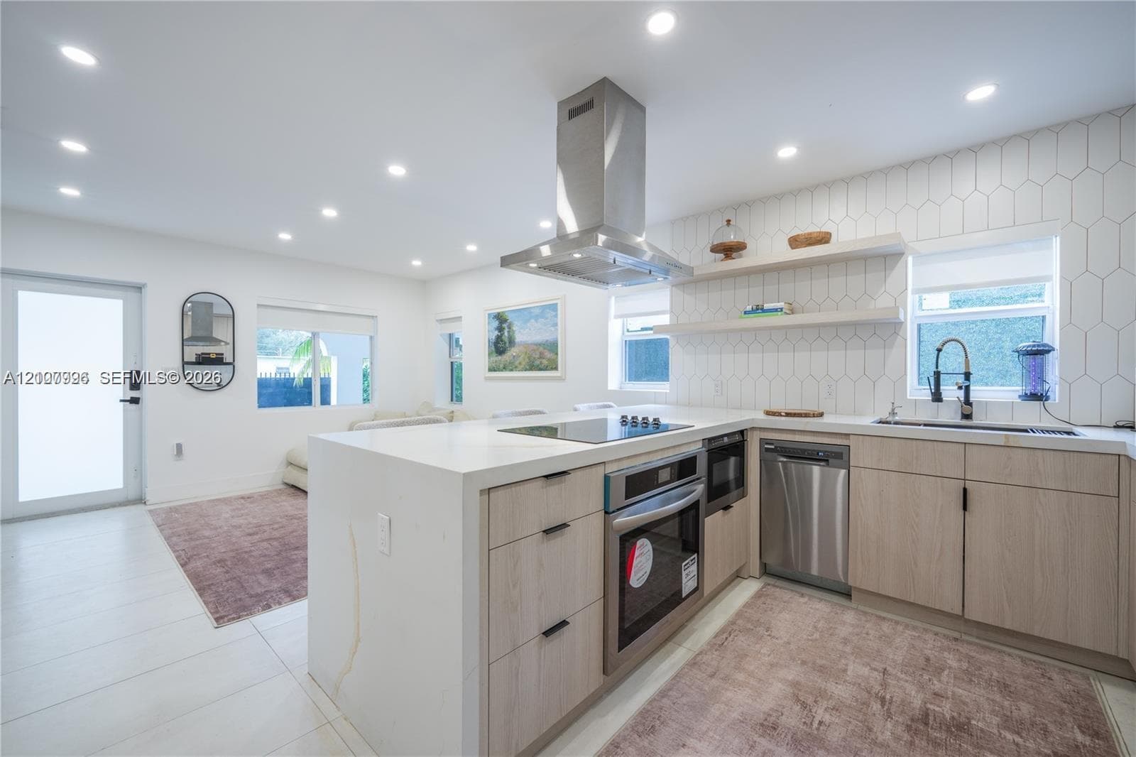 Modern kitchen featuring light-tone wood cabinetry, white stone-finish countertops, stainless steel appliances, a high-reach professional style faucet, and geometric tile backsplash with integrated shelving