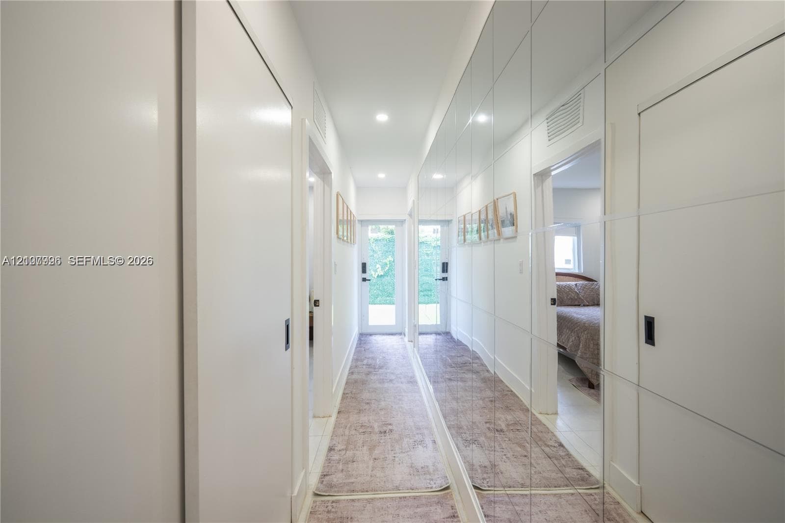 Hallway featuring floor-to-ceiling mirrored wall panels, recessed lighting, and dual glass-panel entry doors