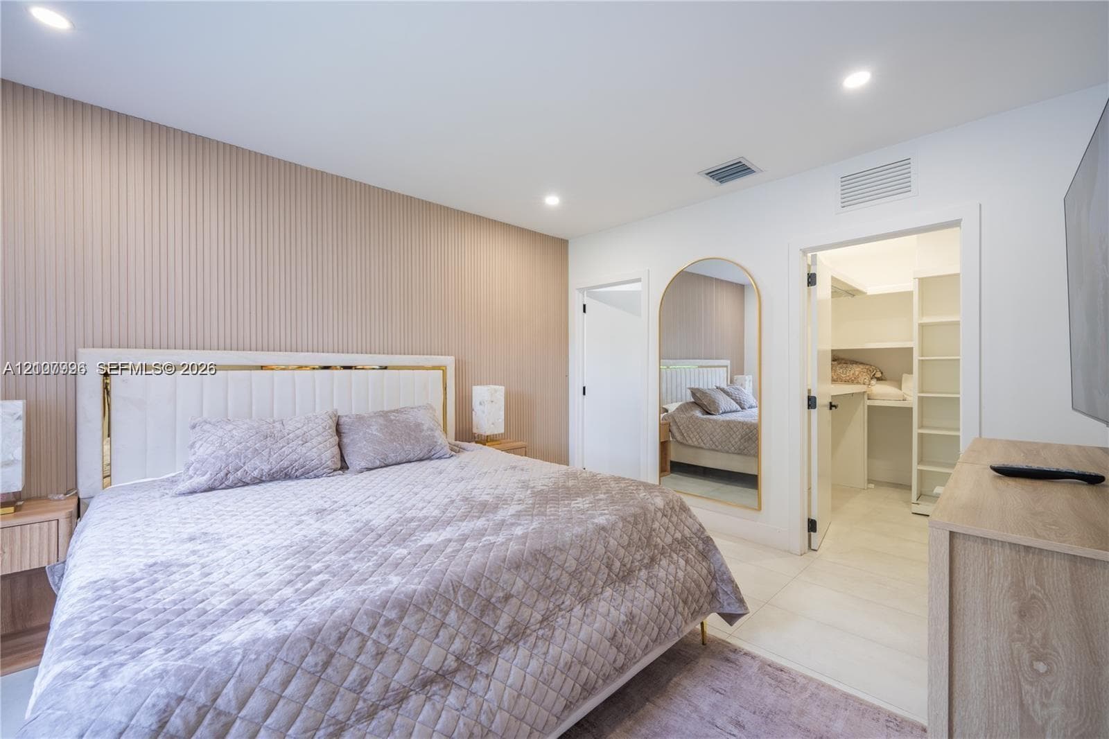 Bedroom featuring a vertical-slat accent wall, recessed ceiling lighting, arched wall mirror, and a walk-in closet with built-in shelving