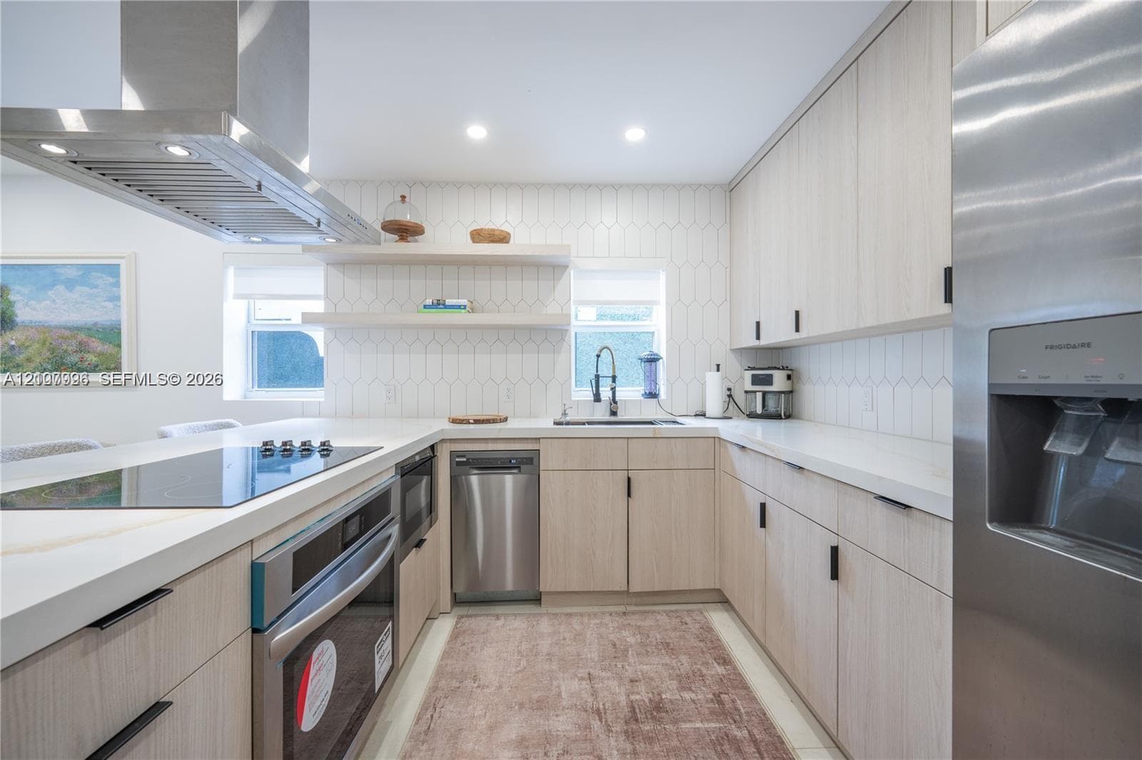 Kitchen featuring light wood-finish cabinetry, white countertops, stainless steel appliances, a stainless steel range hood, and a geometric-tiled backsplash