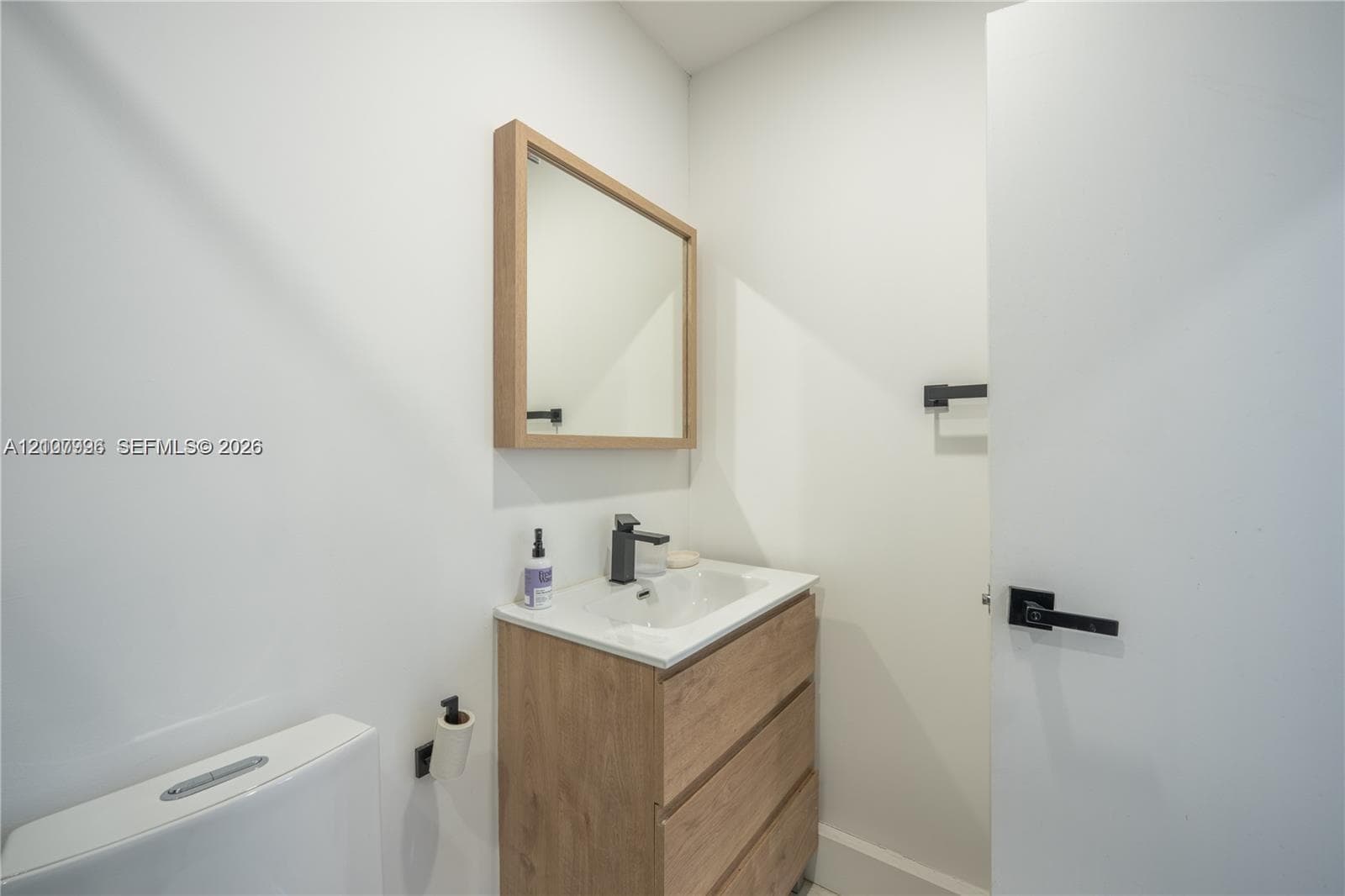 Wood-finish vanity featuring an integrated sink, matte black faucet, wall-mounted mirror with wood frame, and matching matte black hardware