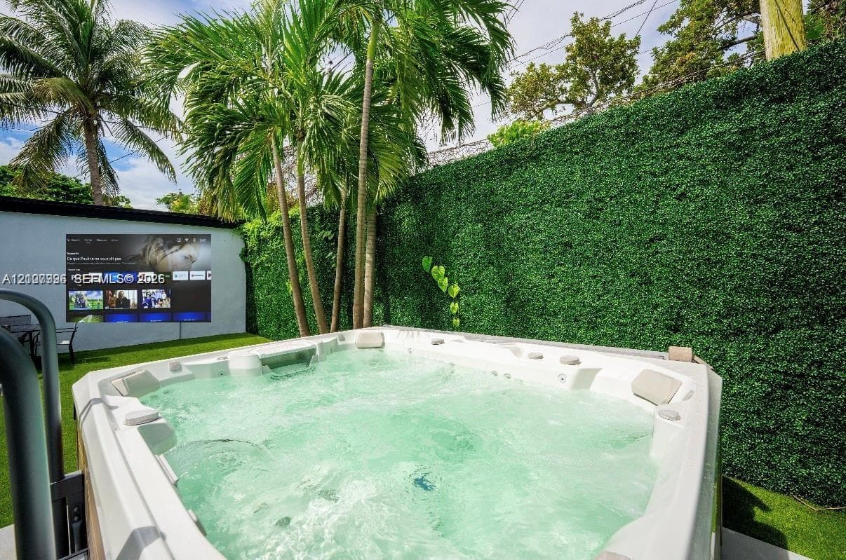 Outdoor space featuring a built-in jetted spa, artificial turf surfacing, and privacy-focused hedge wall