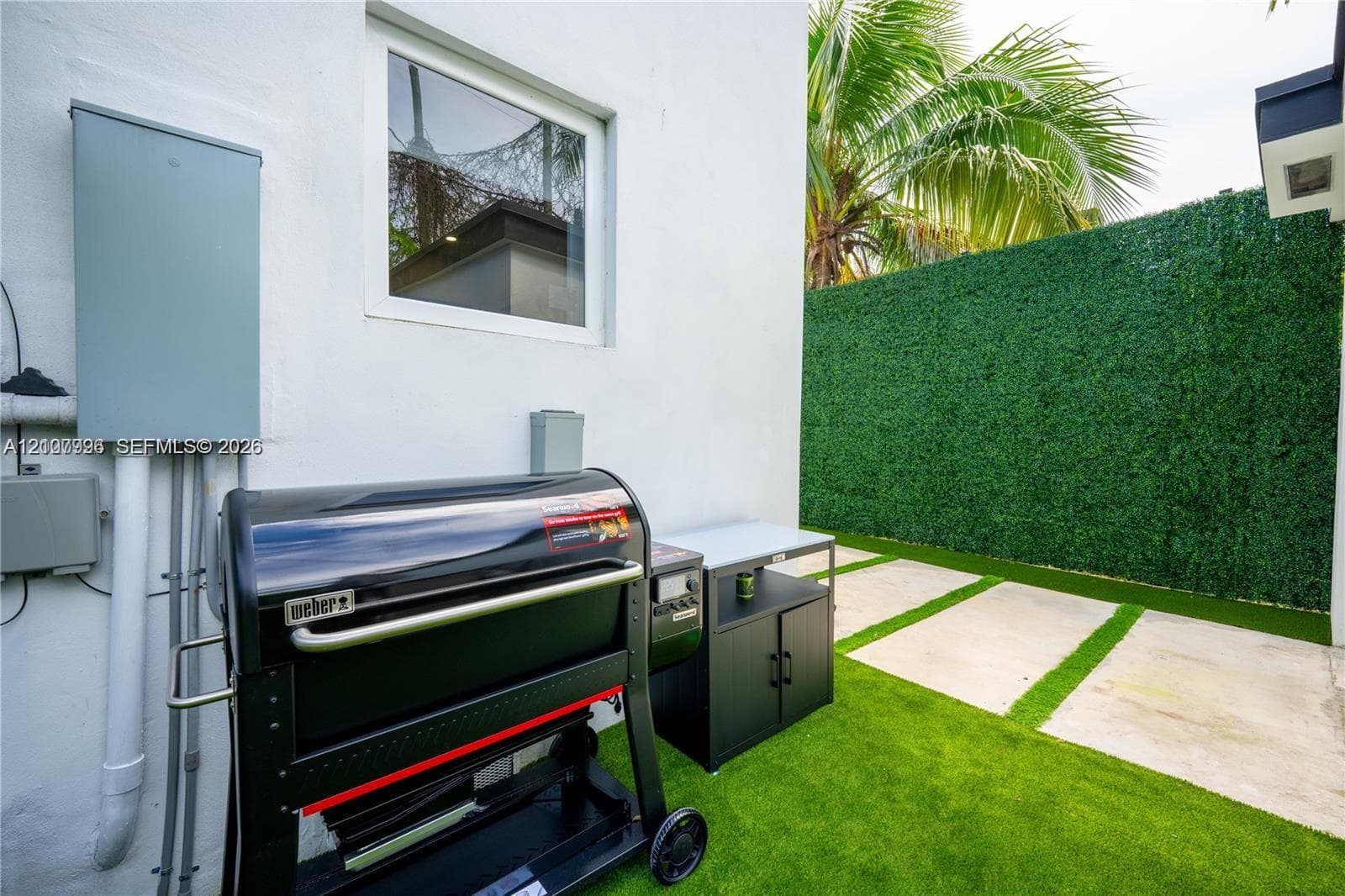 Outdoor space featuring concrete paver stepping stones, artificial turf, and a privacy hedge