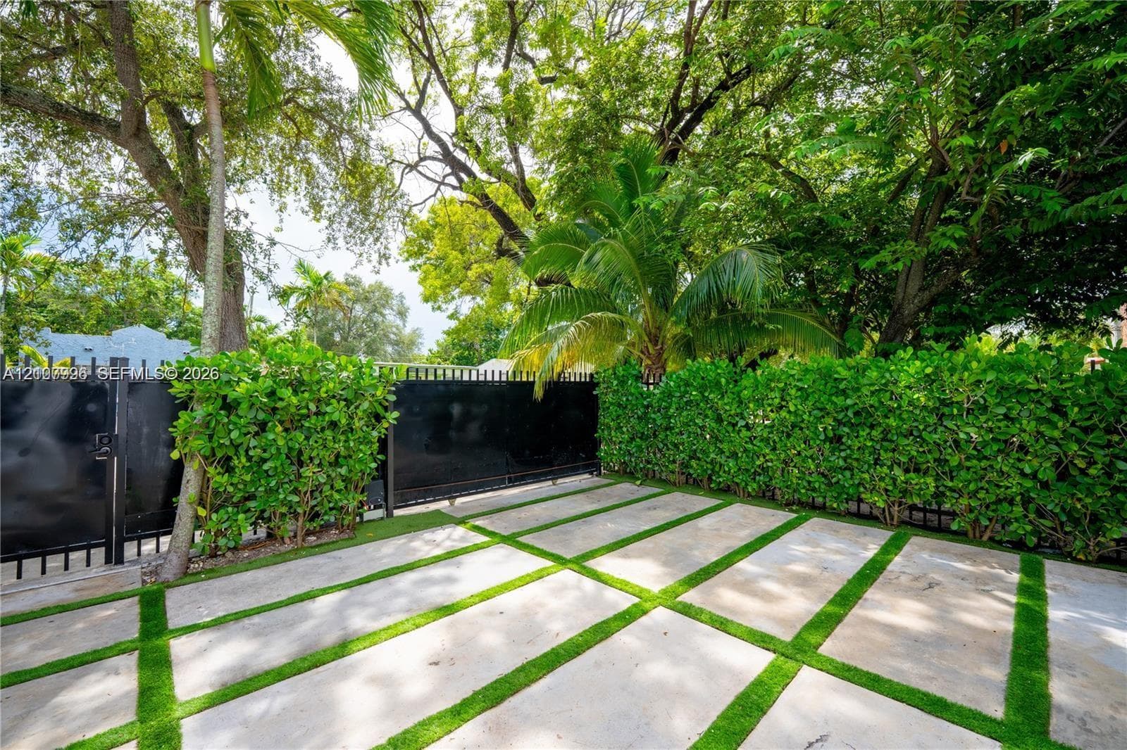 Concrete paver patio with integrated turf grid, enclosed by black metal fencing and mature privacy hedges