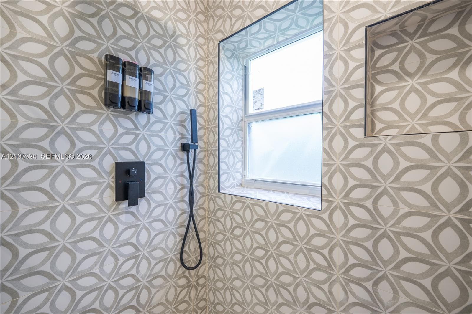 Shower featuring patterned tile wall surround, recessed storage niche, single-hung window, and matte black plumbing fixtures
