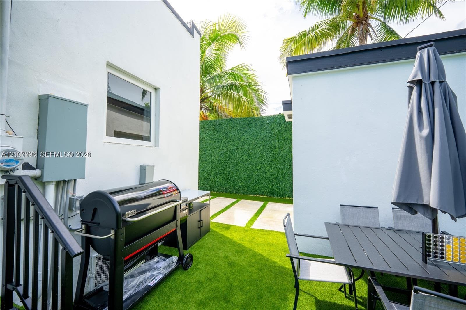 Side courtyard featuring artificial turf, stone paver accents, and a perimeter privacy screen
