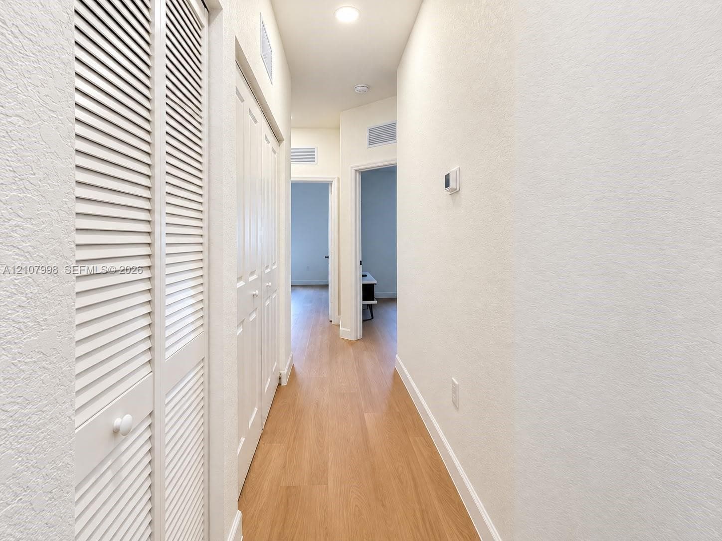 Hallway featuring wood-finish flooring, white louvered-style closet doors, and recessed lighting