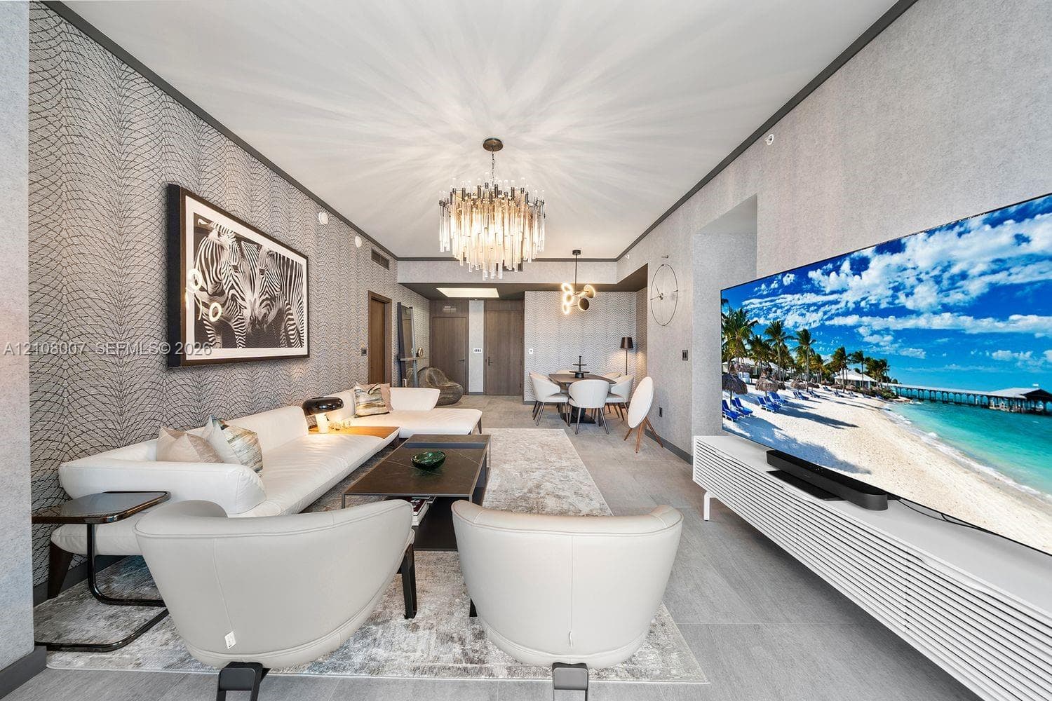 Living area featuring textured wall coverings, multi-tiered crystal chandelier lighting, built-in slatted media cabinetry, and grey tile flooring