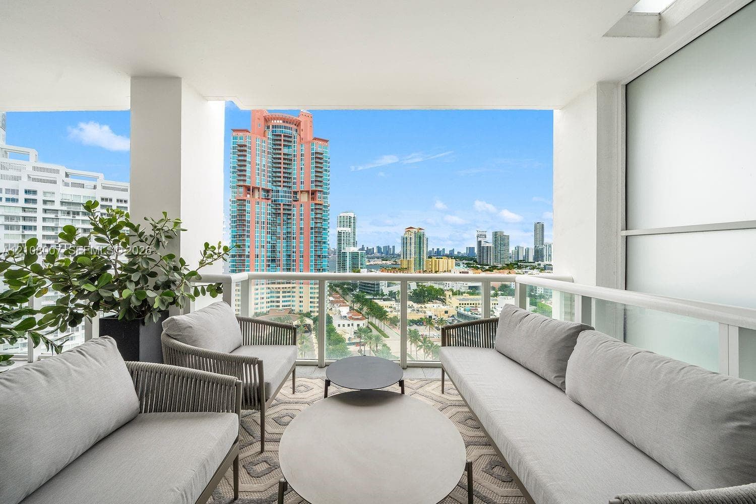 Covered balcony featuring a glass-panel railing, recessed ceiling lighting, and urban skyline backdrop