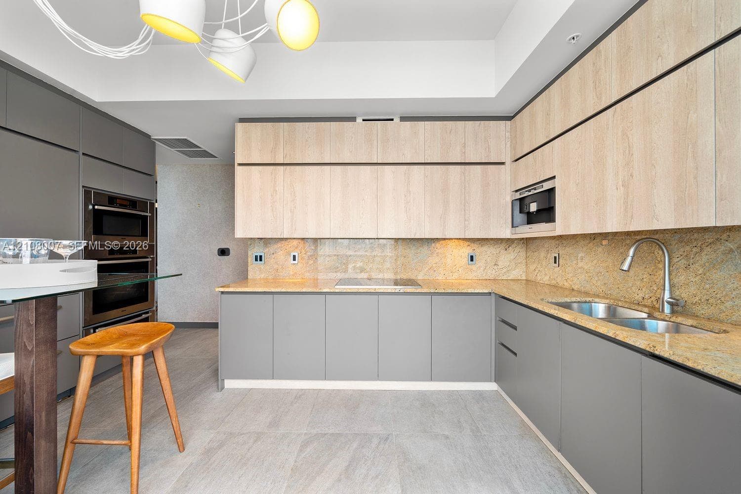 Kitchen featuring two-tone flat-panel cabinetry, stone countertops, integrated wall ovens, a multi-head modern light fixture, and stone-finish flooring