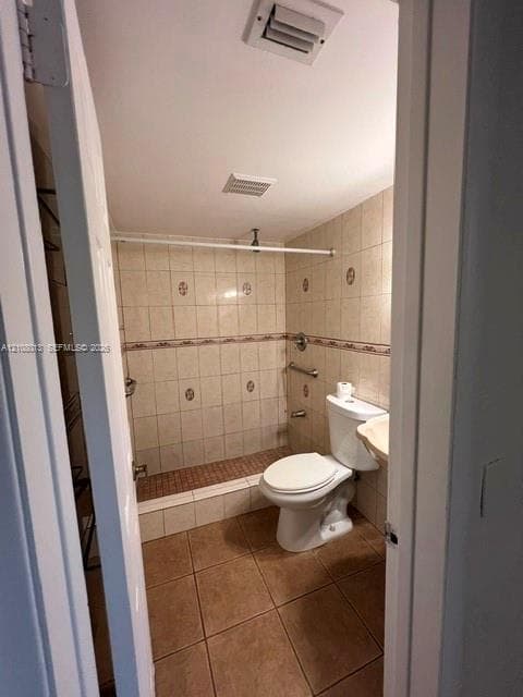 Bathroom featuring square floor tiling, wall-to-wall ceramic tile shower surround with decorative accent border, walk-in shower with mosaic tile flooring, and wall-mounted stainless steel grab bar