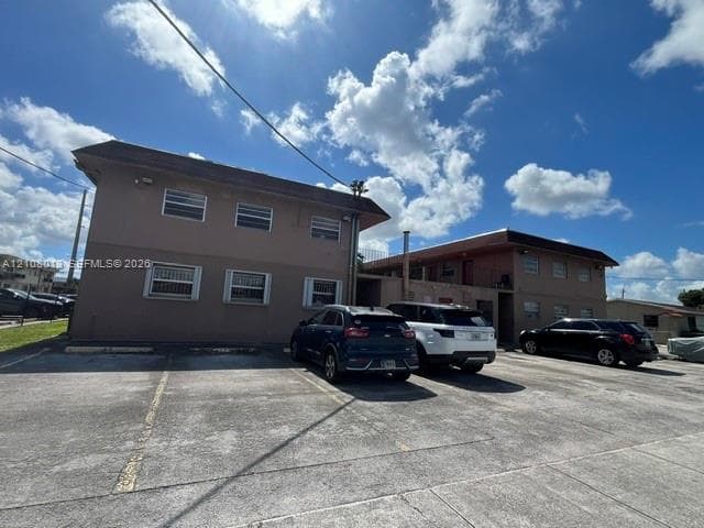 Two-story multi-unit structure featuring concrete exterior walls, horizontal sliding windows, and an asphalt parking area