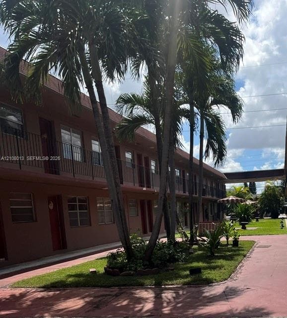 Exterior building facade featuring a two-story design with wrought-iron railings, mature palm trees, landscaped greenery, and paved walkways