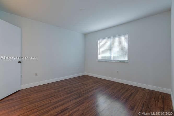 Room interior featuring wood-finish flooring, neutral walls, and a window with horizontal blinds