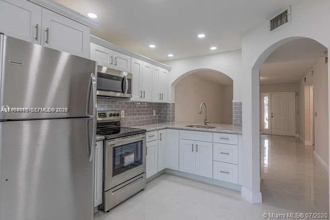 Kitchen featuring white shaker-style cabinetry, stainless steel appliances, tiled backsplash, stone-finish countertops, and recessed lighting