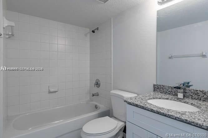 Full bathroom featuring a tub-shower combination with floor-to-ceiling tile surround, vanity with stone-finish countertop, undermount sink, and wall-mounted mirror