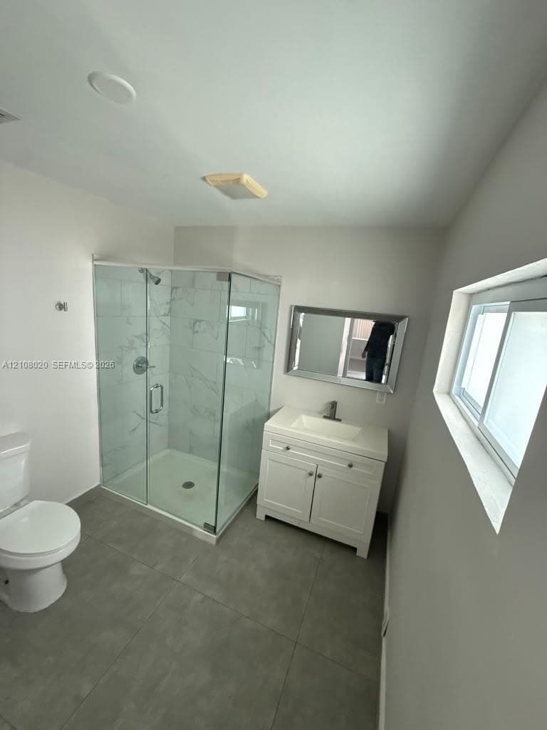 Corner shower enclosure with glass panels and patterned wall tile, white vanity cabinet with a rectangular basin, gray floor tile, and a wall-mounted mirror
