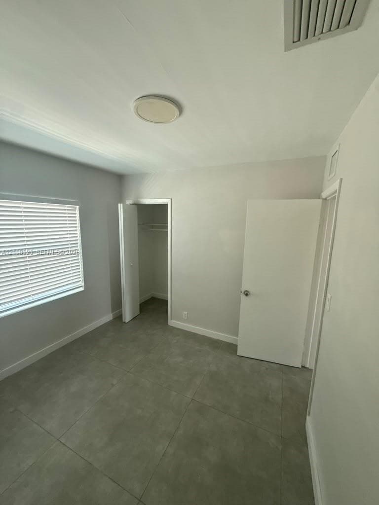 Room featuring large-format ceramic tile flooring, neutral wall paint, and a window with horizontal blinds