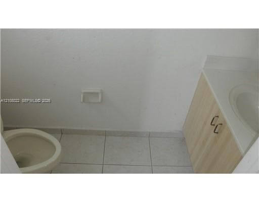 Vanity with light-toned wood-finish cabinetry, integrated countertop with sink, and tile flooring