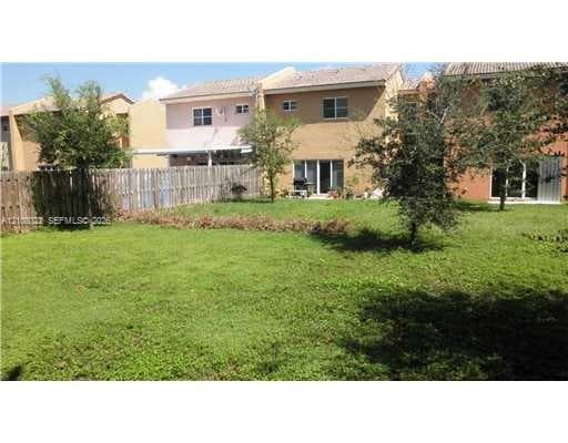 Expansive grassy backyard featuring a wooden privacy fence, mature trees, and ground-level rear access via sliding glass doors