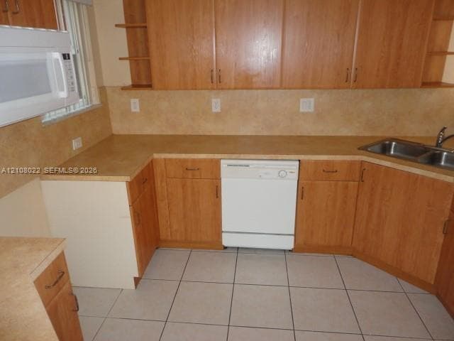 Kitchen featuring natural wood-finish cabinetry, laminate countertops, a stainless steel double-basin sink, a built-in microwave, and tile flooring