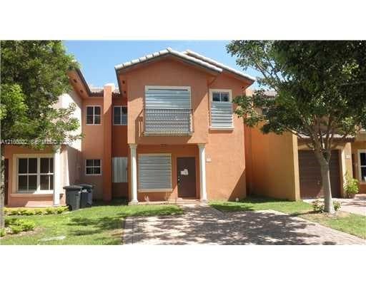 Stucco exterior featuring a second-story balcony with metal railings, a paver driveway, and hurricane shutters