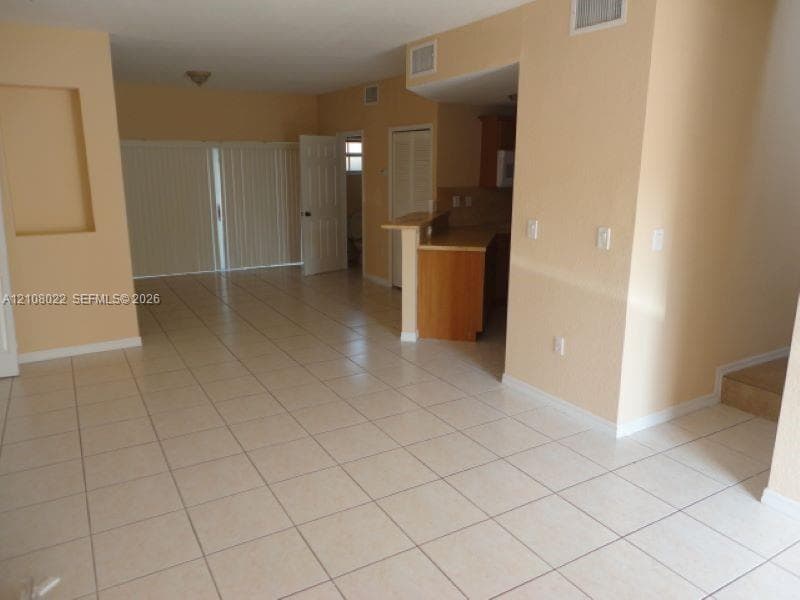 Open-concept interior featuring neutral tile flooring, built-in wall niche, kitchen breakfast bar, and vertical sliding door blinds