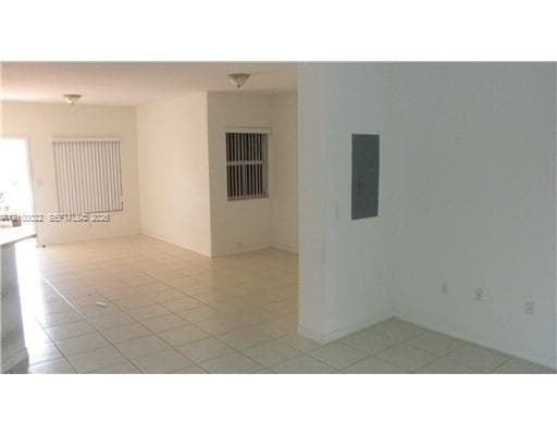 Interior area featuring neutral-tone tile flooring, multiple windows with vertical blinds, flush-mount ceiling lighting, and a recessed electrical panel