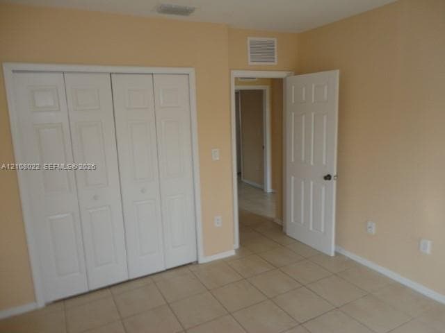Room featuring neutral wall paint, tile flooring, four-panel folding closet doors, and a solid-core six-panel interior door