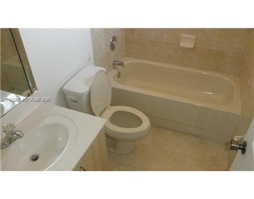 Bathroom featuring an integrated vanity countertop with an oval basin, chrome-finish faucet, tile-surround bathtub, and neutral-tone floor tiling