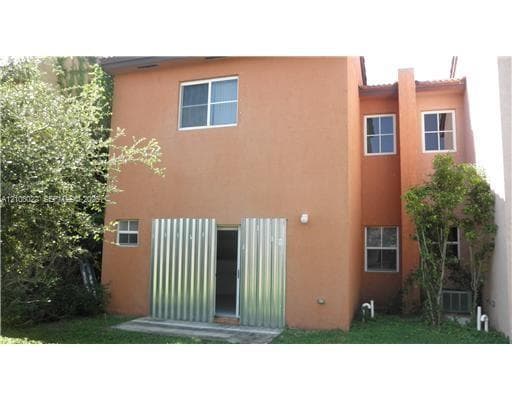 Stucco exterior featuring dual-pane windows, corrugated metal privacy screen, and concrete patio