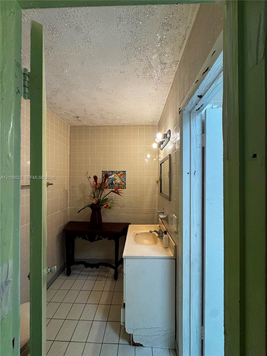 Bathroom featuring floor-to-ceiling wall tile, ceramic floor tiling, a vanity cabinet with an integrated sink, and a wall-mounted light fixture