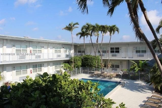 Courtyard swimming pool featuring a paved pool deck, metal safety fencing, mature palm trees, and two-story exterior balcony railings
