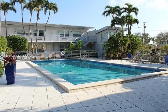 Rectangular swimming pool featuring a tile surround, metal perimeter fencing, and mature palm trees