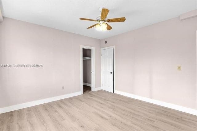 Neutral-toned room featuring wood-finish flooring, a ceiling fan with integrated lighting, and a closet with a solid-panel door