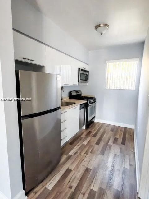 Kitchen featuring white flat-panel cabinetry, stainless steel appliances, wood-finish flooring, and a single-basin undermount sink