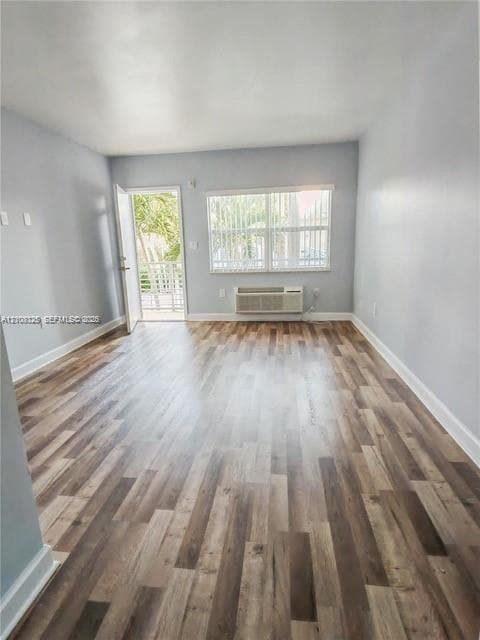 Interior space featuring wood-finish flooring, neutral wall tones, large window with vertical blinds, and a wall-mounted climate control unit