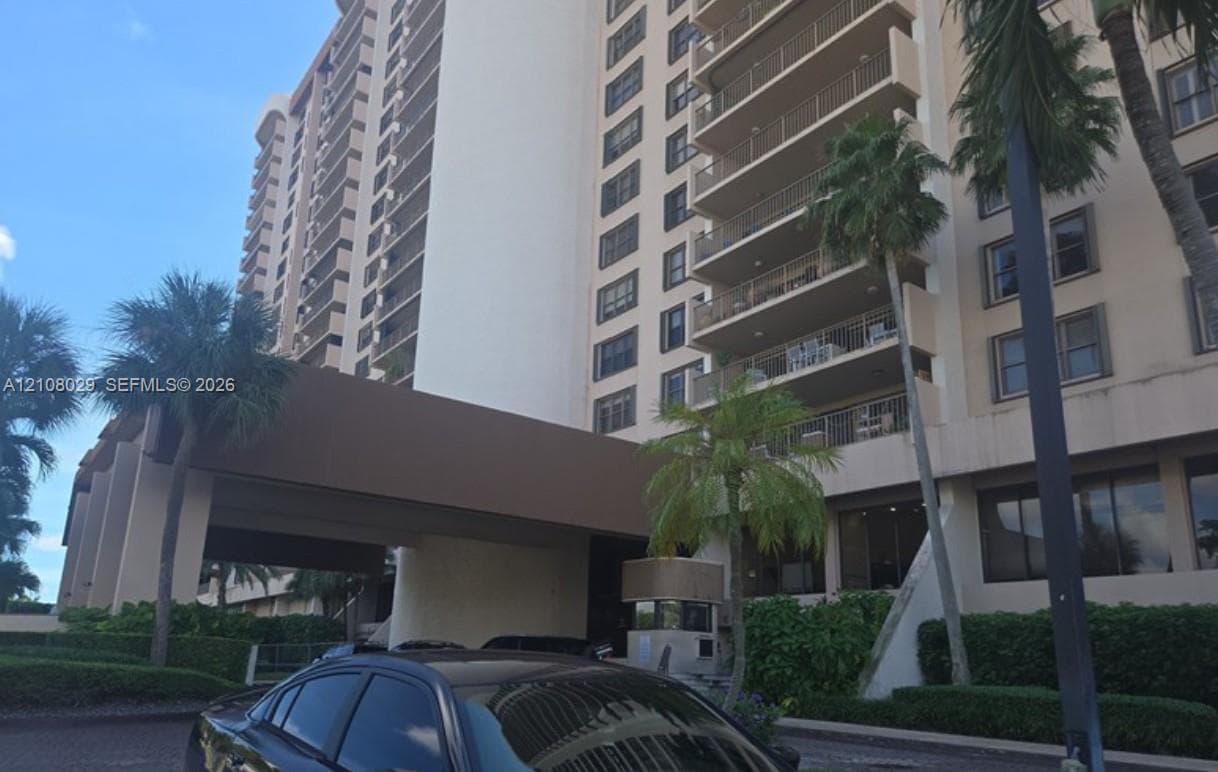 Multi-story high-rise exterior featuring a covered entryway, private balconies, and landscaped tropical plantings